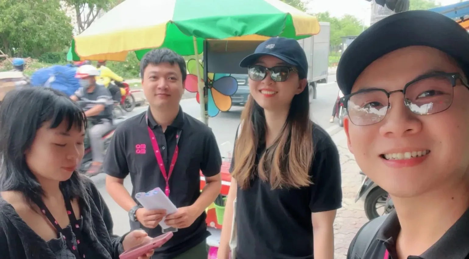 Four colleagues in black company polos and lanyards on a busy street beside a vendor's cart.