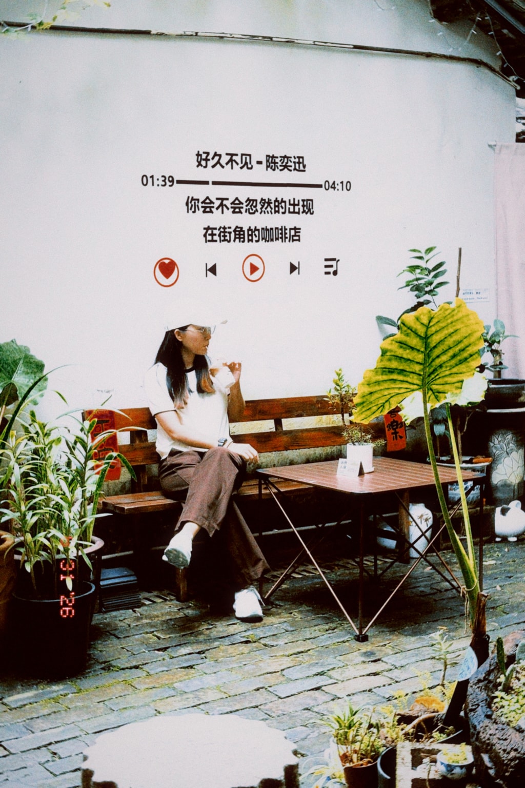 Person seated at a café table surrounded by plants