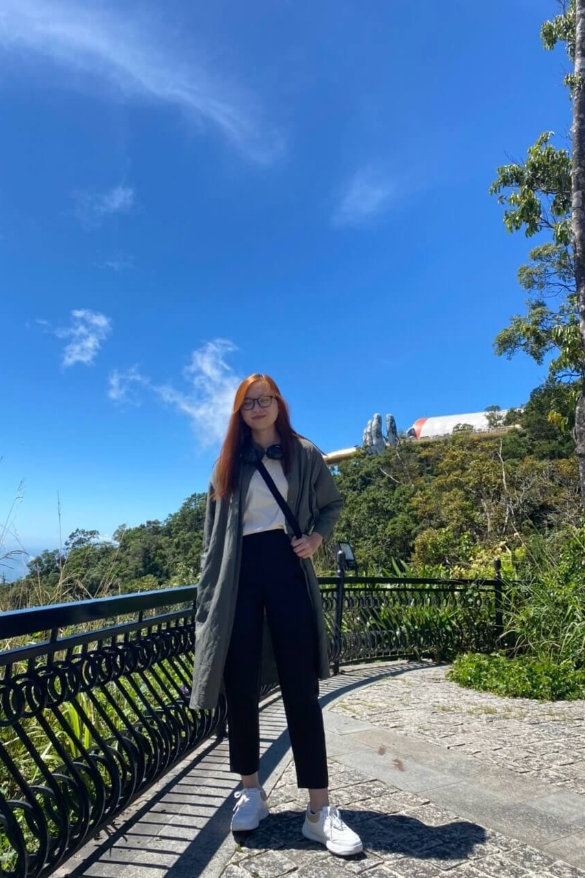 A woman stands full-length with the Golden Bridge in the distance behind her.
